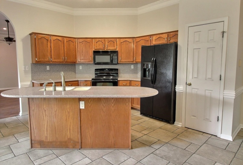 Kitchen with black appliances, brown cabinets, crown molding, ceiling fan, and light tile patterned floors