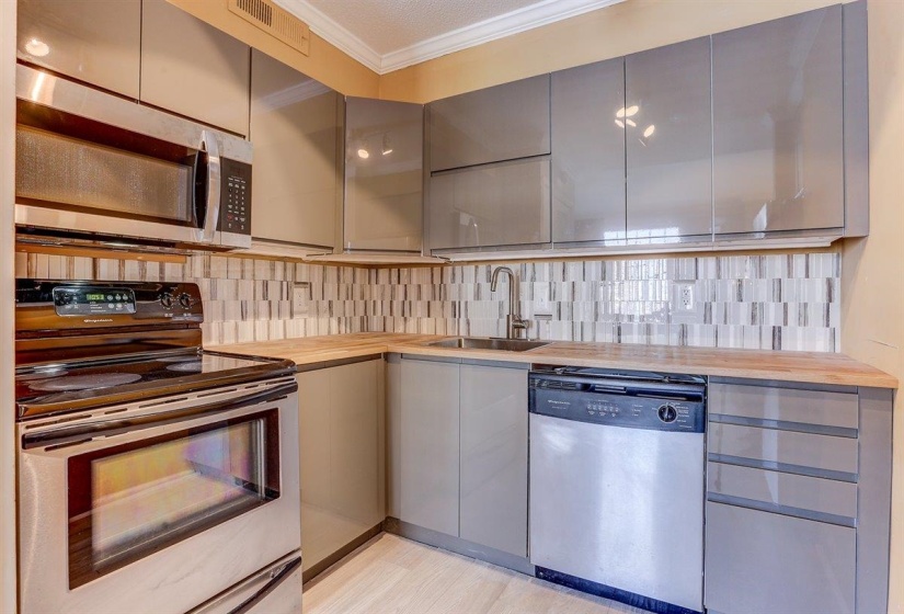 Kitchen featuring appliances with stainless steel finishes, decorative backsplash, gray cabinets, ornamental molding, and wooden counters