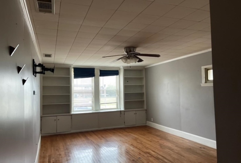 Spare room featuring ornamental molding, wood-type flooring, a ceiling fan, and built in shelves