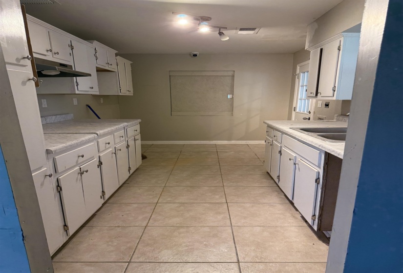 Kitchen featuring under cabinet range hood, light countertops, light tile patterned flooring, and white cabinets