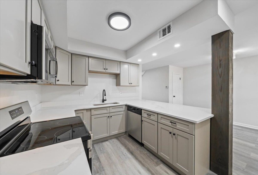 Kitchen with gray cabinetry, stainless steel appliances, light wood-type flooring, recessed lighting, and a peninsula
