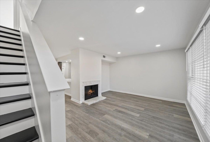 Unfurnished living room featuring stairs, wood finished floors, a fireplace, and recessed lighting