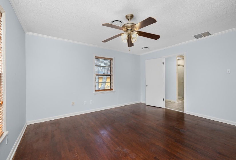Empty room featuring dark wood-type flooring, crown molding, a textured ceiling, and ceiling fan