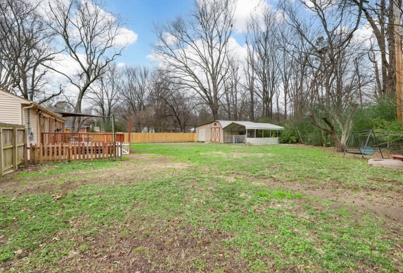 Fenced backyard featuring an outdoor structure and a carport