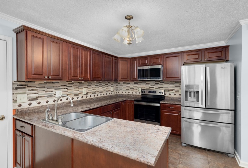 Kitchen with stainless steel appliances, ornamental molding, a textured ceiling, a chandelier, and hanging light fixtures