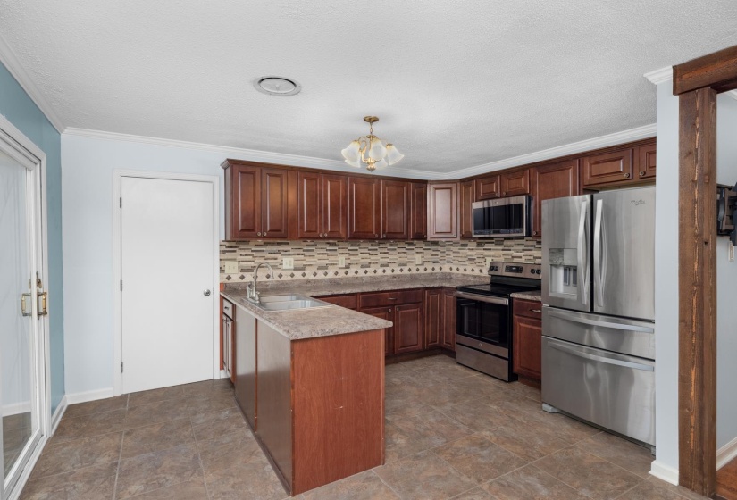 Kitchen featuring stainless steel appliances, a chandelier, ornamental molding, decorative backsplash, and stone finish flooring