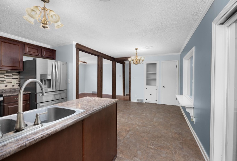 Kitchen featuring a chandelier, stainless steel fridge, a textured ceiling, crown molding, and tasteful backsplash