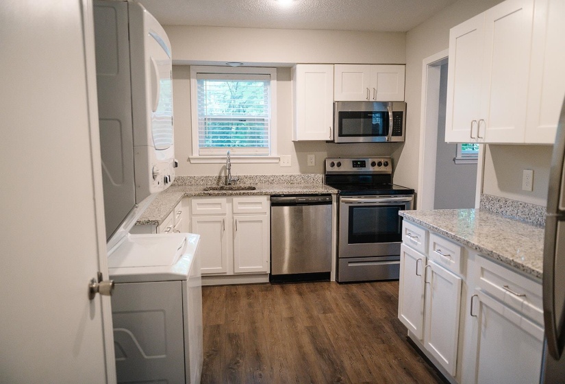 Kitchen featuring white cabinets, stainless steel appliances, dark hardwood / wood-style flooring, stacked washing maching and dryer, and sink