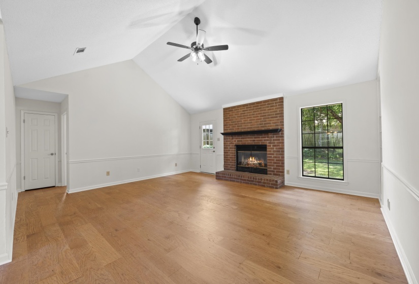 living room featuring a ceiling fan, vaulted ceiling, a brick fireplace, and light wood-style flooring
