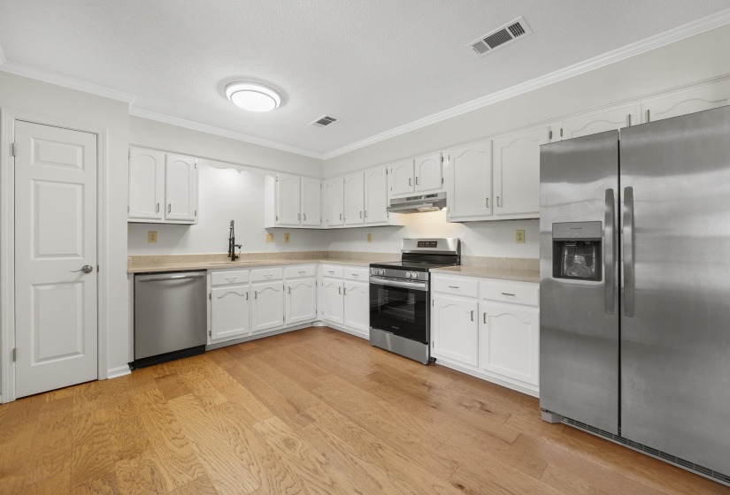 Kitchen with appliances with stainless steel finishes, under cabinet range hood, ornamental molding, quartz countertops, and white cabinets