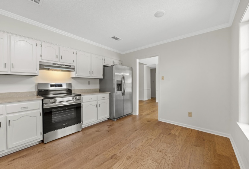 Kitchen with stainless steel appliances, under cabinet range hood, crown molding, white cabinets, and light wood-style floors