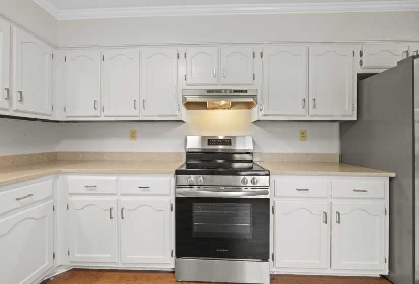 Kitchen with appliances with stainless steel finishes, under cabinet range hood, white cabinets, crown molding, and quartz countertops