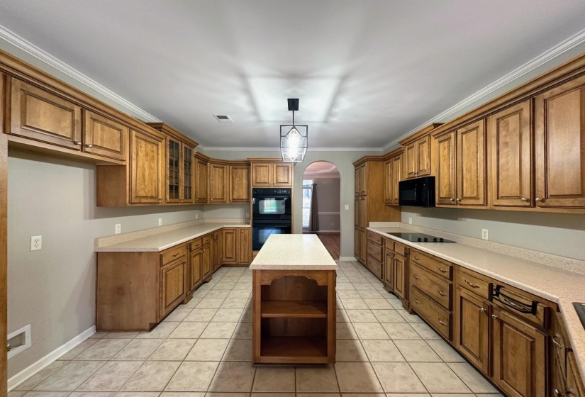 Kitchen featuring brown cabinets, arched walkways, open shelves, light countertops, and ornamental molding