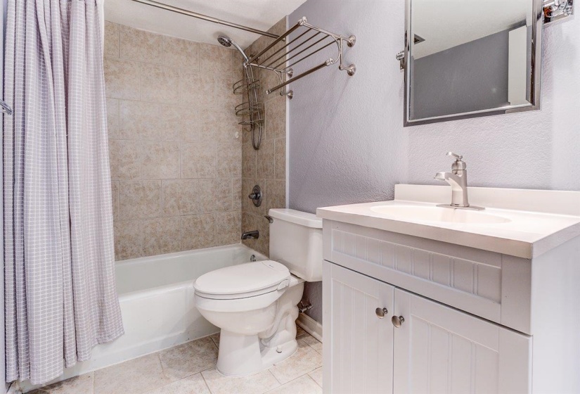 Bathroom featuring a textured wall, shower / bath combination with curtain, vanity, and light tile patterned flooring