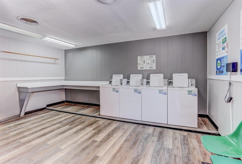 Community laundry with a textured ceiling, independent washer and dryer, and wood walls