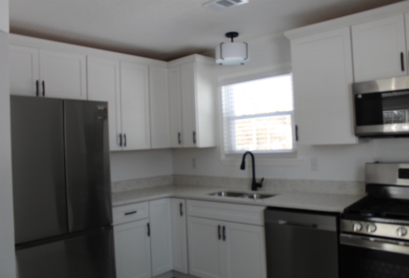 Kitchen with appliances with stainless steel finishes, white cabinets, and light stone countertops