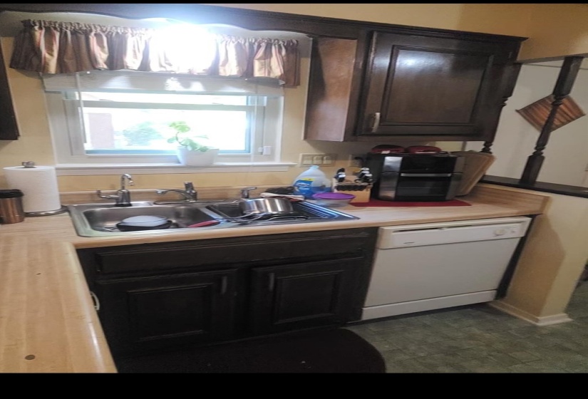 Kitchen with light countertops, white dishwasher, and dark brown cabinets