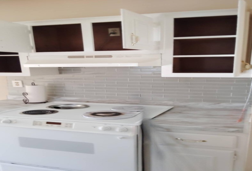 Kitchen view of white electric range, white cabinets, under cabinet range hood, and open shelves