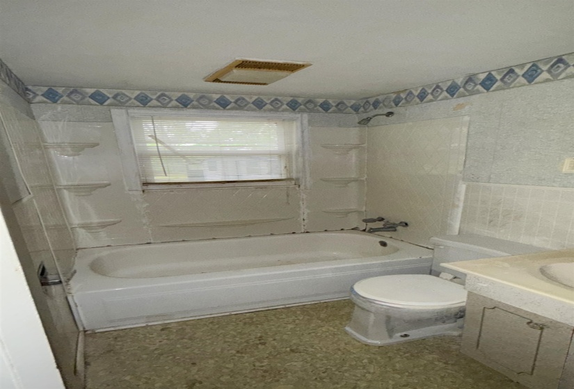 Bathroom featuring a built-in bathtub with shower, a window, and a vanity with an integrated sink