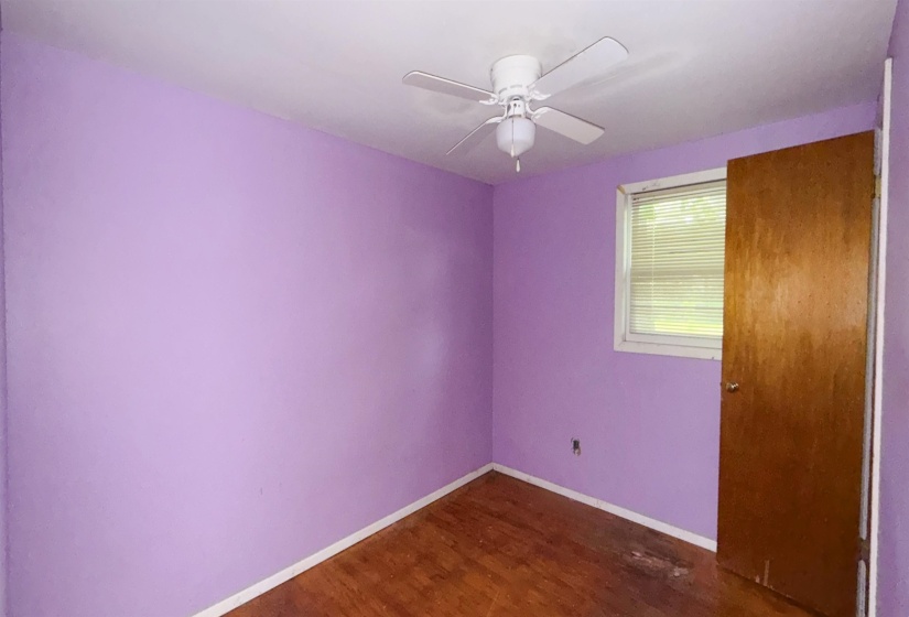 Room with lavender-painted walls, wood-finish flooring, a white ceiling fan with integrated lighting, and a single window with blinds