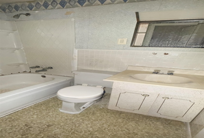 Bathroom featuring a white bathtub with a showerhead, a white toilet, and a vanity with an integrated sink