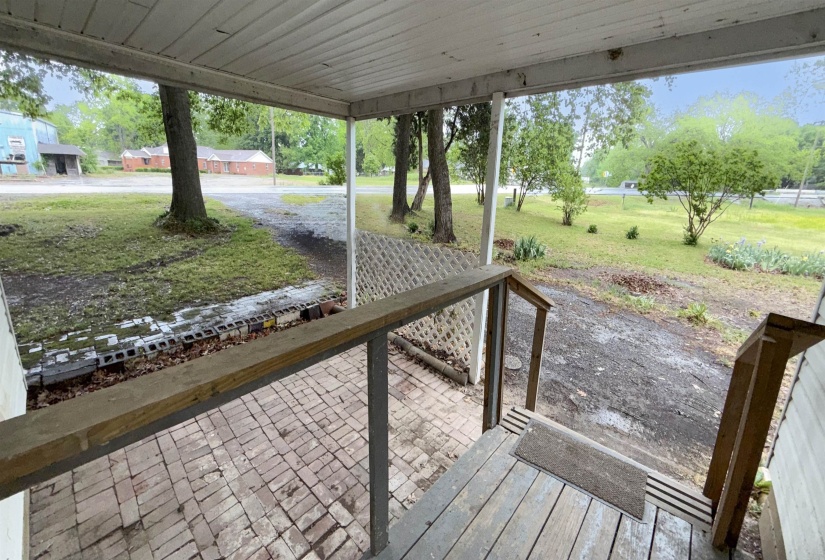 Covered front porch featuring a brick paver floor, wood railing, and lattice privacy screen