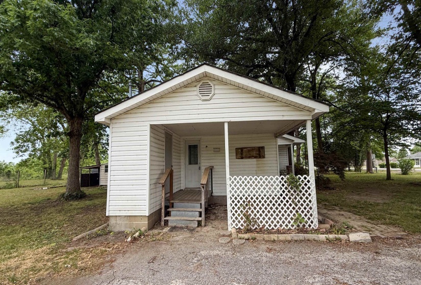 White siding residence featuring a covered front porch, wood-tone steps, and a decorative lattice panel