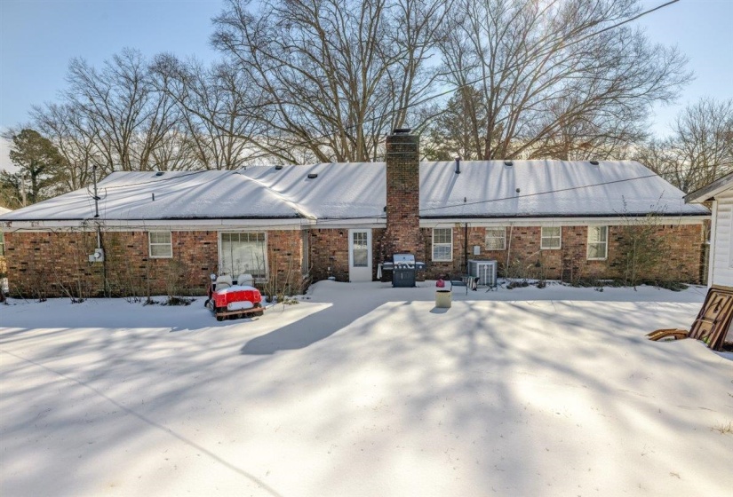 Snow covered rear of property with a chimney, brick siding, and a patio