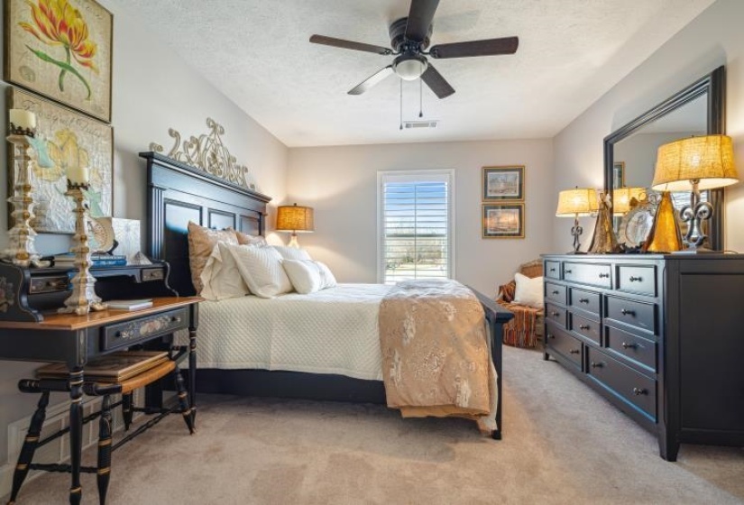 Bedroom featuring ceiling fan, visible vents, a textured ceiling, and light colored carpet