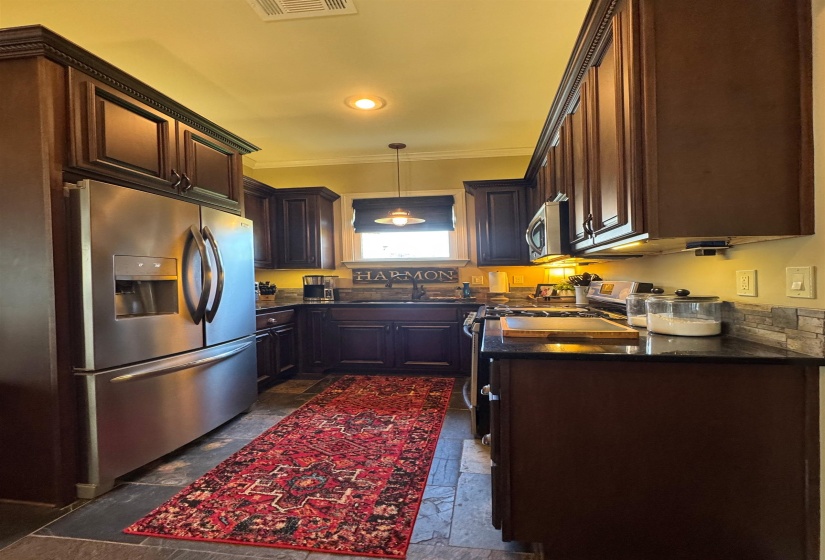 Kitchen featuring appliances with stainless steel finishes, stone tile flooring, dark countertops, crown molding, and pendant lighting