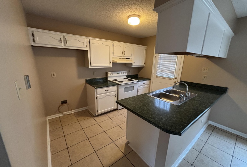 Kitchen featuring dark countertops, electric range, a textured ceiling, white cabinets, and under cabinet range hood
