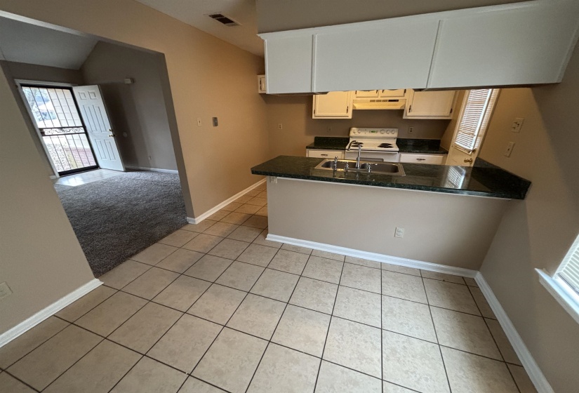 Kitchen featuring light tile patterned floors, white range with electric cooktop, vaulted ceiling, a peninsula, and light carpet
