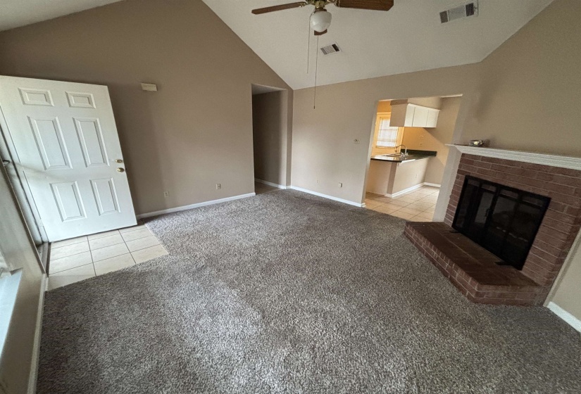 Unfurnished living room with light tile patterned floors, a brick fireplace, light carpet, high vaulted ceiling, and ceiling fan