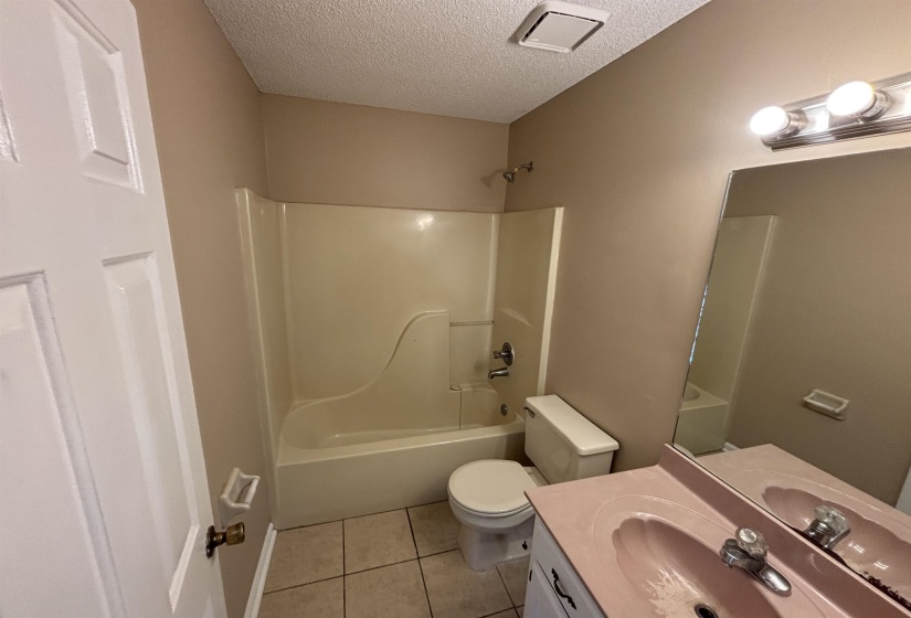 Bathroom featuring vanity, shower / bathtub combination, light tile patterned flooring, and a textured ceiling