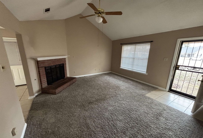 Unfurnished living room featuring light colored carpet, a fireplace, a ceiling fan, light tile patterned flooring, and high vaulted ceiling