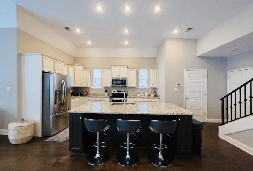Two tone kitchen featuring stainless steel appliances, light stone counters, a kitchen island with sink, a breakfast bar, and a high ceiling