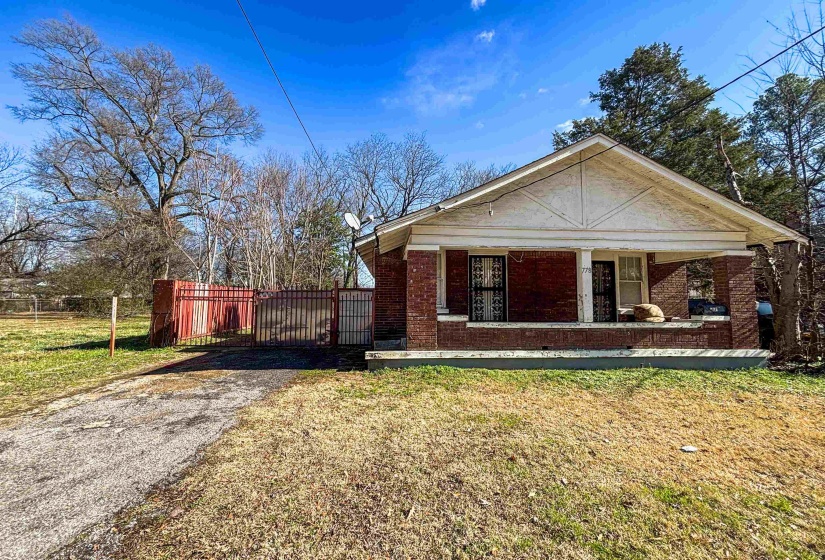 View of front of property featuring covered porch, asphalt driveway, brick siding, and a gate