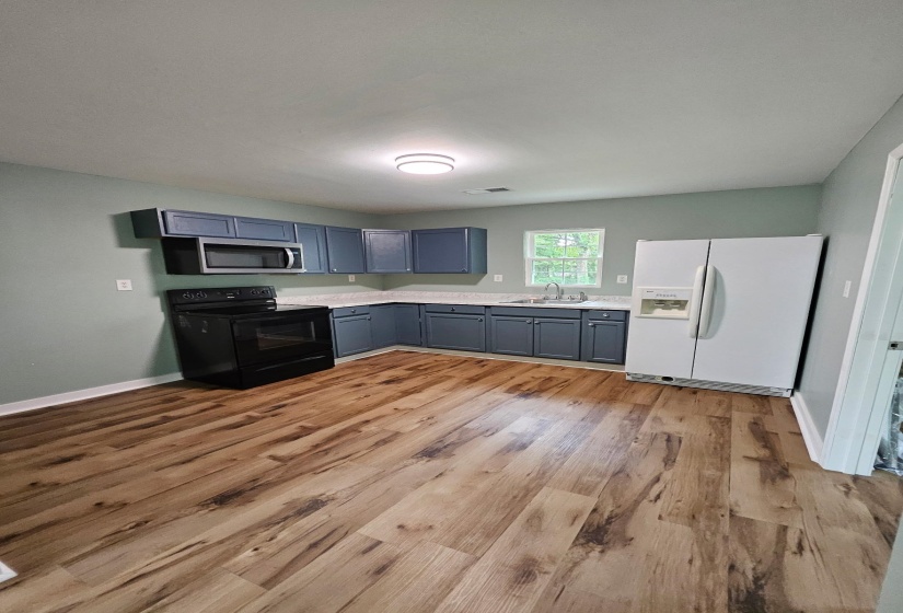 Kitchen featuring black / electric stove, white refrigerator with ice dispenser, blue cabinets, light wood-style floors, and light countertops