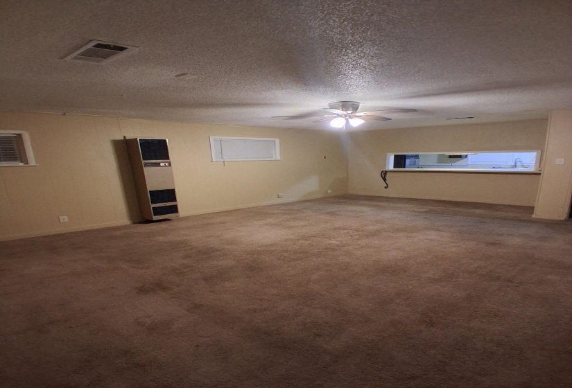 Empty room with carpet floors, a heating unit, a textured ceiling, and a ceiling fan