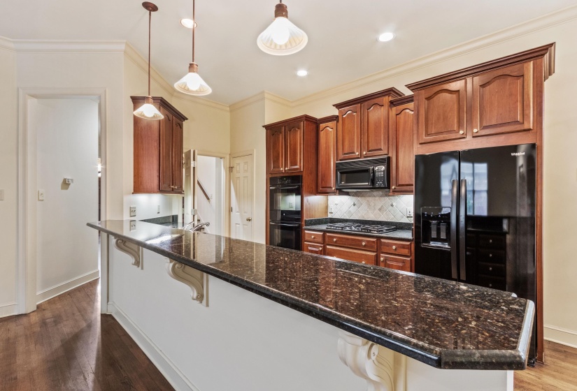 Kitchen featuring extensive dark stone countertops, rich wood cabinetry, stainless steel gas cooktop, built-in double ovens, and wood-finish flooring