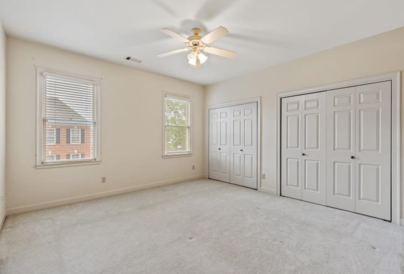 Carpeted room featuring two windows with blinds, a ceiling fan with light fixture, and two sets of bi-fold closet doors