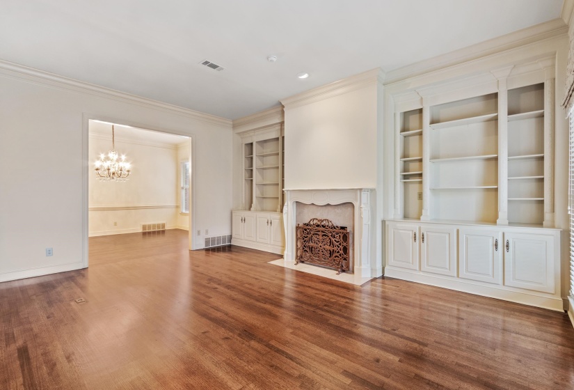 Living area featuring rich wood-finish flooring, built-in shelving with lower cabinetry, a detailed fireplace with an ornate screen, gas logs.
