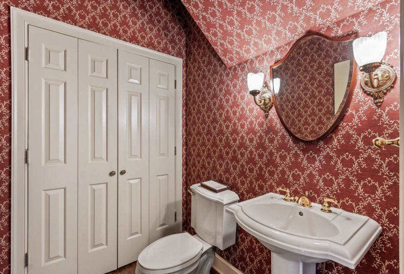 Pedestal sink with gold-tone fixtures, complemented by antique mirror and ornate wall sconces