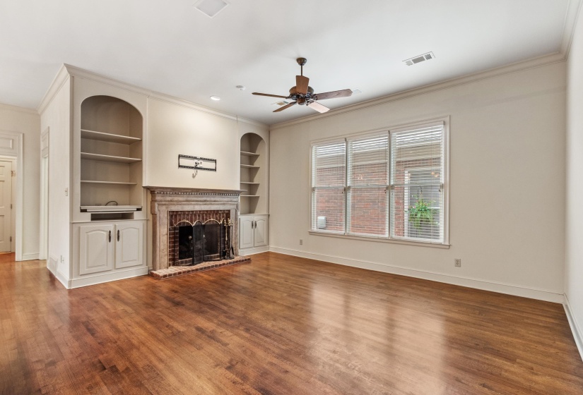 Spacious room featuring wood-finish flooring, a decorative fireplace (gas) with a stone mantel, and built-in shelving with lower cabinetry