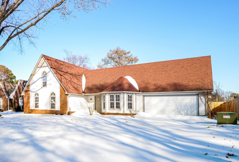 View of front facade with roof with shingles, brick siding, and a garage