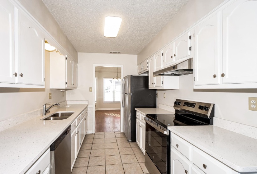 Kitchen featuring stainless steel appliances, light stone countertops, a textured ceiling, white cabinetry, and light tile patterned flooring
