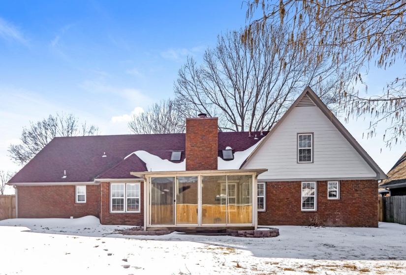 Snow covered back of property featuring brick siding, a sunroom, and a chimney