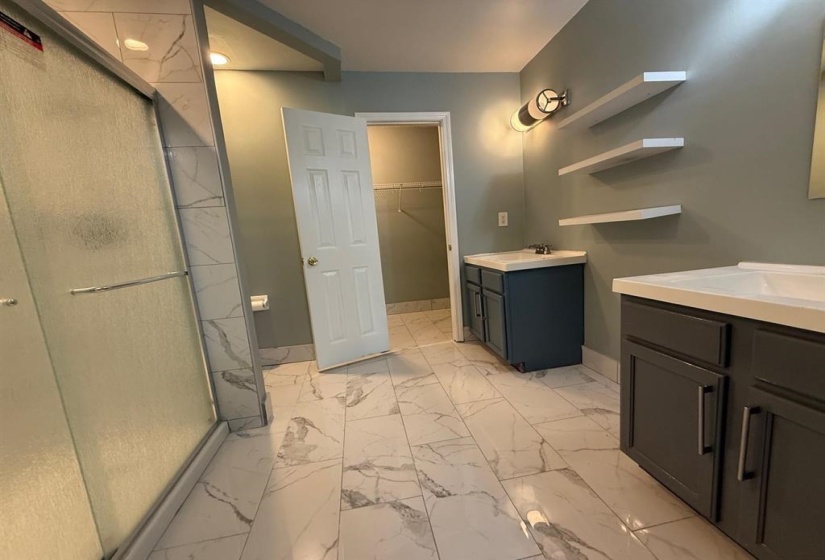 Bathroom with two vanities, a shower stall, light marble finish flooring, and a walk in closet