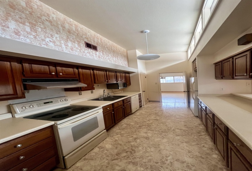 Kitchen featuring white appliances, light countertops, dark wood finish cabinetry, a high ceiling, and pendant lighting