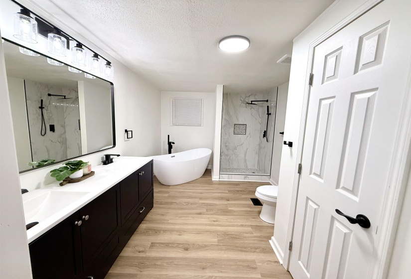 Full bath featuring a marble finish shower, double vanity, light wood-style flooring, a freestanding bath, and a textured ceiling